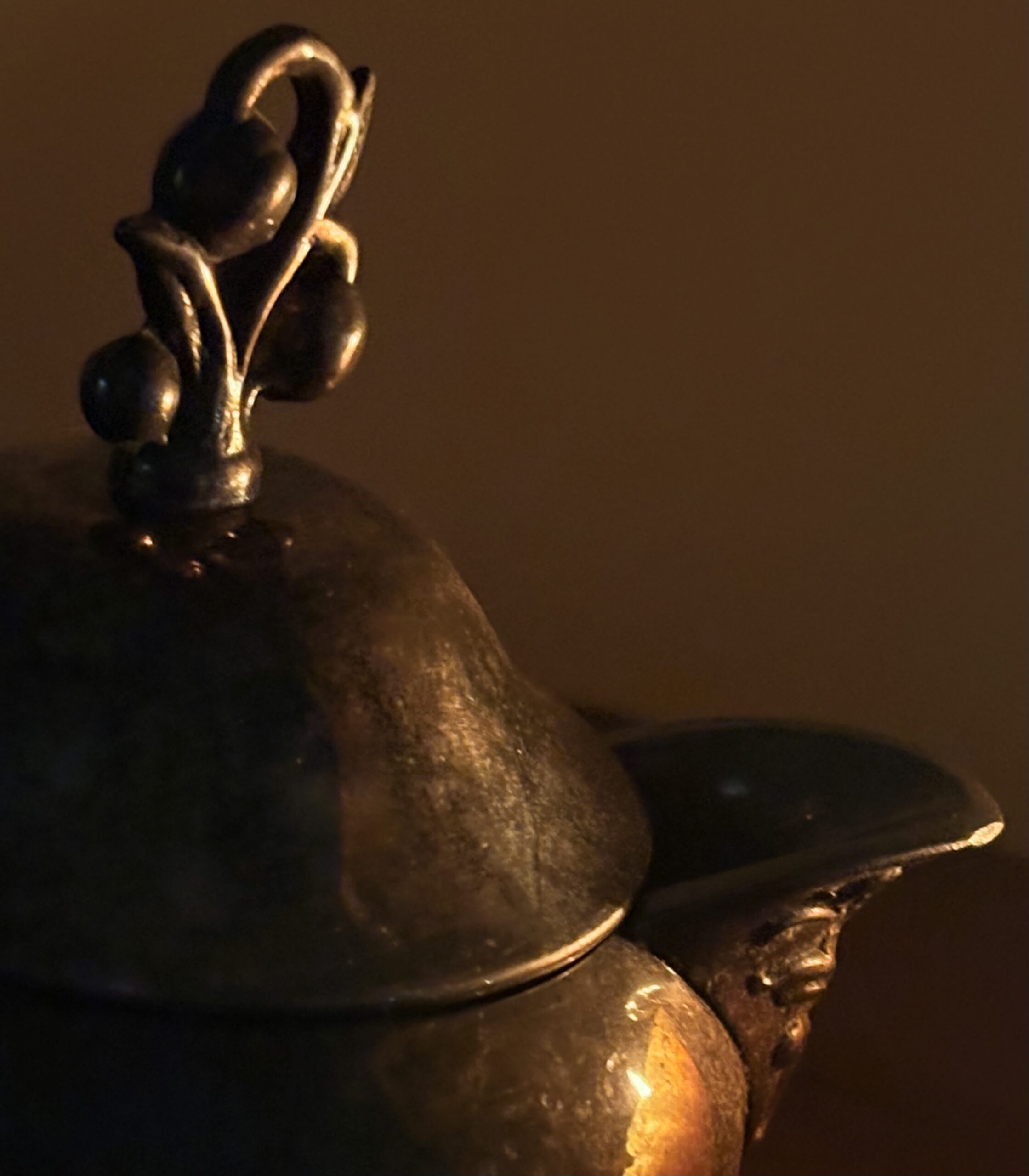 A lidded metal vessel in low light, one side lit gold, the rest in shadow.