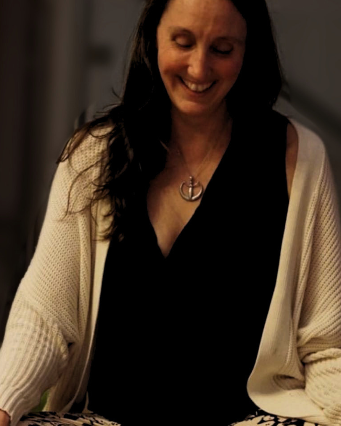 Kristine in warm candlelight, eyes lowered, smiling, seated while working.